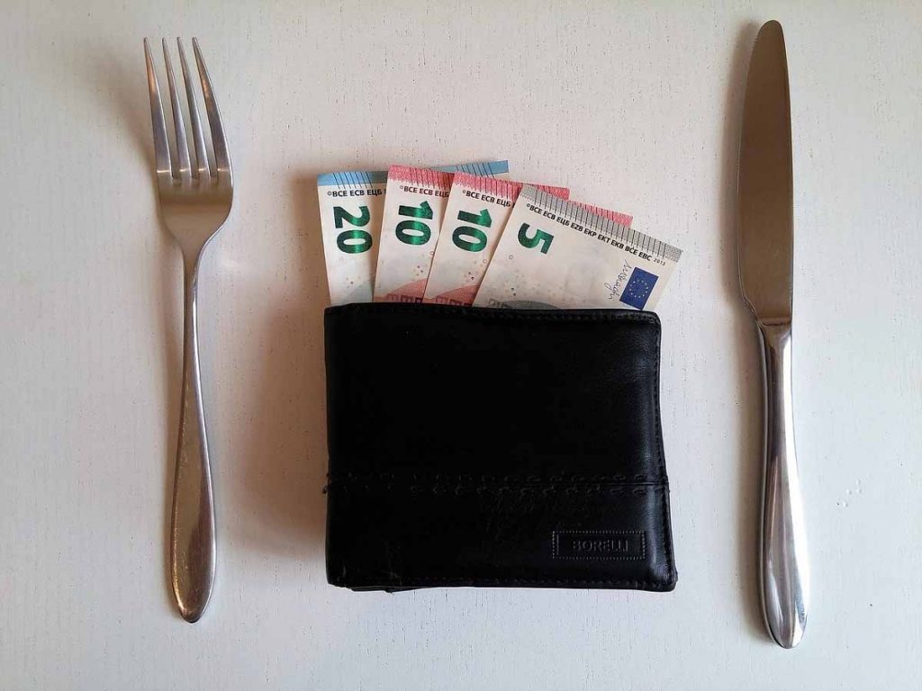 Een volle portemonnee met geld als bord en bestek ernaast.