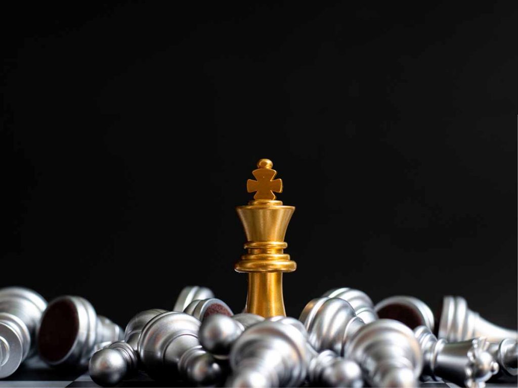 Gouden koning uit het schaakspel staat rechtop terwijl alle andere zilveren stukken zijn omgevallen.