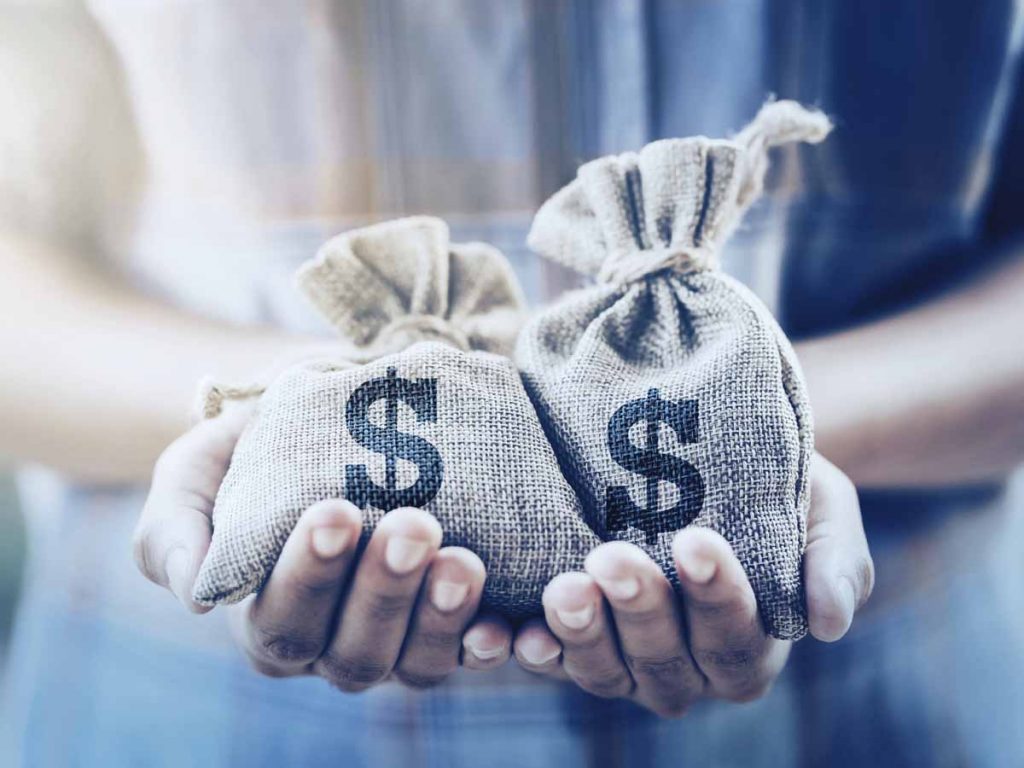 Iemand die twee juten zakken vasthoudt met dollartekens erop.