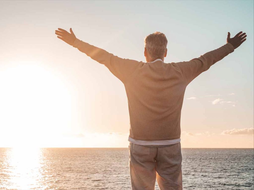 Man van middelbare leeftijd die met z'n armen gespreid op het strand staat.