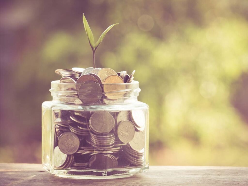 Potje met geld op een houten tafel. Uit het potje groeit een plantje.